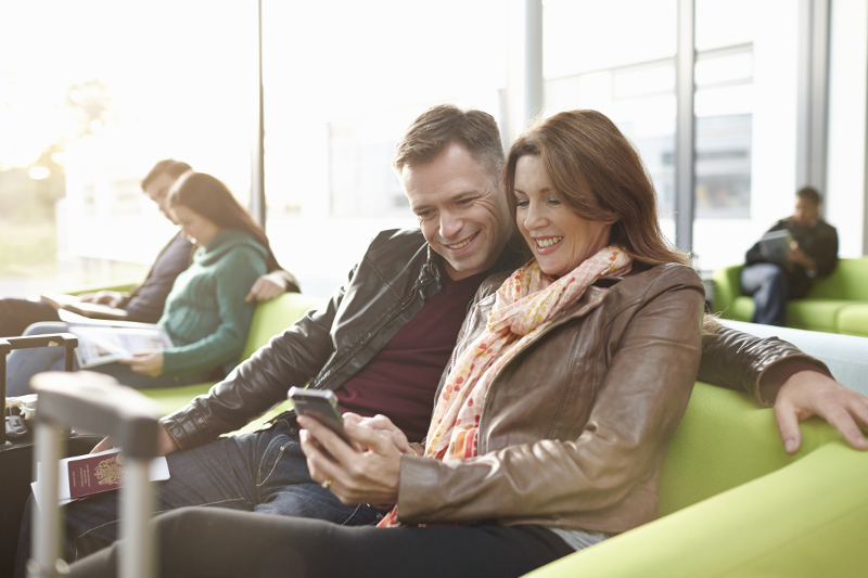 Couple sits in airport looking at mobile phone together