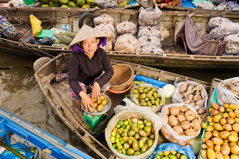 A vendor sells fruit from her boat at a Vietnamese floating market