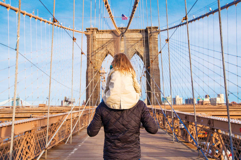 Girl rides on father's shoulders over bridge